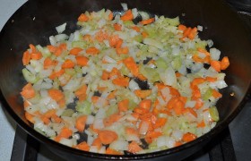 А под сковородой меняем огонь на средний, засыпаем нашинкованные морковь, лук, сельдерей, добавляем  кусочек сливочного масла,  пассеруем  5-7 минут. 