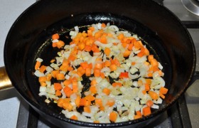 А в сковороду засыпаем лук, снижаем огонь до среднего и пассеруем лук, помешивая, 4-5 минут. Добавляем морковь и обжариваем еще 4-5 минут.