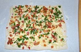 Раскатываем тесто до толщины 3-4 мм, посыпаем сыром, луком, беконом.