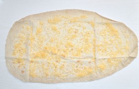 Развернув первый лист лаваша, засыпаем его натертым сыром.