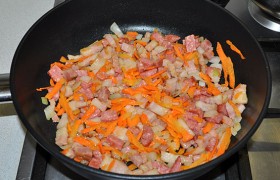 Нарезаем лук, натираем морковь, засыпаем в сковороду и обжариваем еще 5-6 минут. Помешиваем.