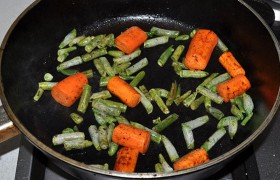 А на сковороде 2-3 минуты с помощью лопатки перекатываем крупно нарезанную морковь, чтобы она подпеклась со всех сторон. Добавляем замороженную стручковую фасоль, перемешиваем еще минуты полторы.