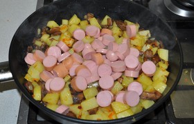 Нарезаем и кладем в сковороду сосиски. Продолжаем обжаривать и перемешивать, пока картошка приготовится.