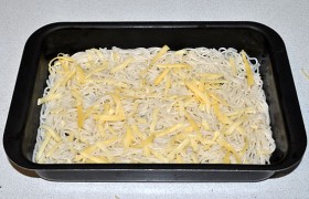 Пасту откидываем на дуршлаг. Половину пасты выкладываем слоем на дно формы, предварительно промазанной растительным или сливочным маслом. И посыпаем частью сыра.