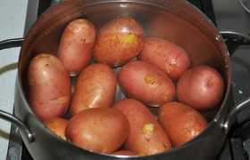 Картофелины качественно промываем под струей воды. Кладем в кастрюлю, доводим до кипения и варим, снизив огонь, 5-6 минут. Сливаем горячую воду, картошка немного подсыхает и остывает.