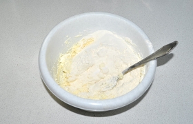 Масло, которое мы заранее нарезали, размягчается быстро. Перемешиваем его с творогом, посыпаем разрыхлителем (содой), солью, всыпаем просеянную муку, вымешиваем до однородности.