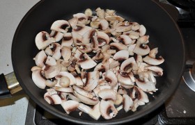 На сковородке рядом разогреваем масло, кладем нарезанные грибы, жарим 4-5 минут.