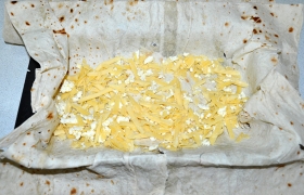 Выбираем форму (её промазываем маслом) и размещаем в ней один лаваш так, чтобы он стал как бы формой для пирога, а по бокам оставались свисающие края. Промазываем его заливкой. Посыпаем слоем тертого сыра.