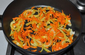 Ставим на разогрев большую толстодонную сковороду с маслом или латку. Полукольцами шинкуем лук, натираем морковь. На огне чуть выше среднего, помешивая лопаткой,  пассеруем  до прозрачности – 5-6 минут. 