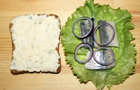 На два ломтика кладем салатные листы, кусочки сельди и колечки лука. Можно добавить еще по листу салата.