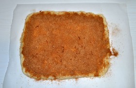 Раскатываем или разминаем тесто в прямоугольник (удобно прямо на листе пекарской бумаги). Насыпаем ровным слоем начинку из растертых вместе корицы и оставшегося сахара.