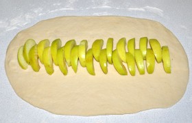 Раскатываем тесто в длинный овал, толщина – 4-5 мм. Нарезанные ломтиками яблоки выкладываем рядком посередине и посыпаем корицей, сахаром или сахарной пудрой.