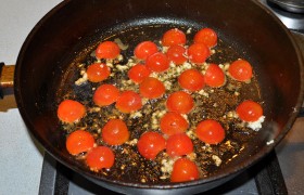 А в ту же сковороду, не меняя среднего огня, кладем порезанные на половинки помидоры черри и выдавливаем через пресс чеснок.  Пассеруем  пару минут, накрываем и отставляем с конфорки. 