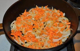 Огонь конфорки снижаем до среднего, на сковороду добавляем сливочное масло и засыпаем нарезанный половинками колец лук и крупно тертую морковку. Пассеруем, порой помешивая, 7-8 минут.
