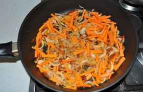 Первым делом мелко нарезаем грудинку и выкладываем на разогревающуюся сковороду – пусть вытапливается жир. Можем обойтись и просто парой ложек растительного масла. Добавляем нарезанные грибы. Шинкуем морковь и луковицу, сладкий перец, вместе с обжаренной грудинкой и шампиньонами держим на среднем огне 10 минут 
