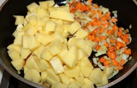 Сковороду с маслом ставим греться на среднем огне,  шинкуем  лук и морковь. Лук обжариваем 3-4 минуты, выкладываем морковь. Нарезаем кусочками-кубиками очищенную картошку, через 3-4 минуты после моркови добавляем в сковороду.