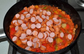 Снимаем с сосисок оболочку, нарезаем кружками, добавляем в сковороду с овощами, перемешиваем. 