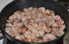 Сковороде с маслом даем раскалиться на сильном огне, выкладываем мясо и 3-4 минуты, все время перемешивая, обжариваем до смены цвета мяса на светлый и появления корочек. Мясо убираем в посуду для тушения (латку).