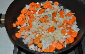 А на сковороду высыпаем нарезанные лук и морковь, корень петрушки, еще снижаем – до среднего – огонь, 7-9 минут овощи томятся, лук становится прозрачным – 