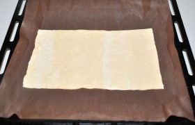 Размороженное тесто раскладываем на столе и делим пополам. Одну половину перекладываем на противень, подстелив коврик для выпечки или пекарскую бумагу.