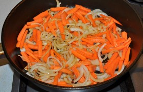 Нашинкованный половинками колец лук засыпаем в сковороду, регулятор огня – на средний, пассеруем 5 минут, помешивая, добавляем тонкие брусочки моркови.